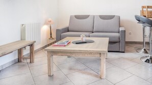 Un rincón acogedor con un sofá gris, una mesa de centro de madera, un pequeño banco de madera y una lámpara de pie.