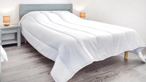 Una cama bien hecha con edredón blanco, dos lámparas de noche y un cabecero de madera.