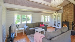A cozy living room with a fireplace, wooden floors, and a large window. - 3 bedroom gorgeous home in Gedser (Gedser)