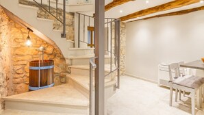 Una scala con un muro in pietra e una botte di legno, che conduce a una sala da pranzo con tavolo e sedie.