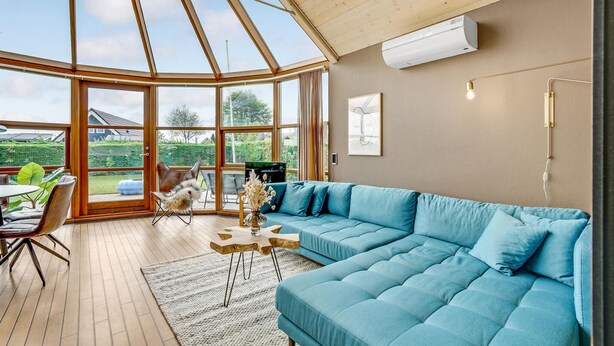 A modern living room with a large blue sectional sofa, a wooden coffee table, and a glass dining table with chairs.