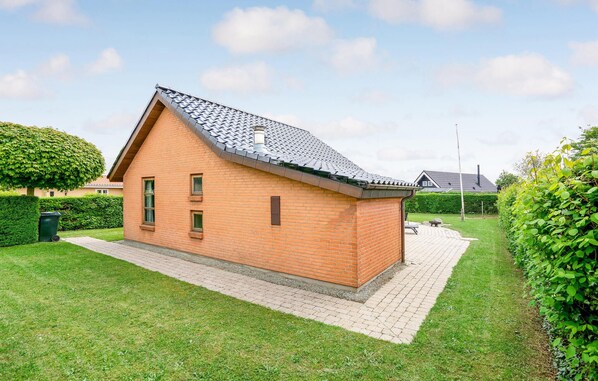 A small brick house with a sloped roof, a paved driveway, and a well-maintained lawn.