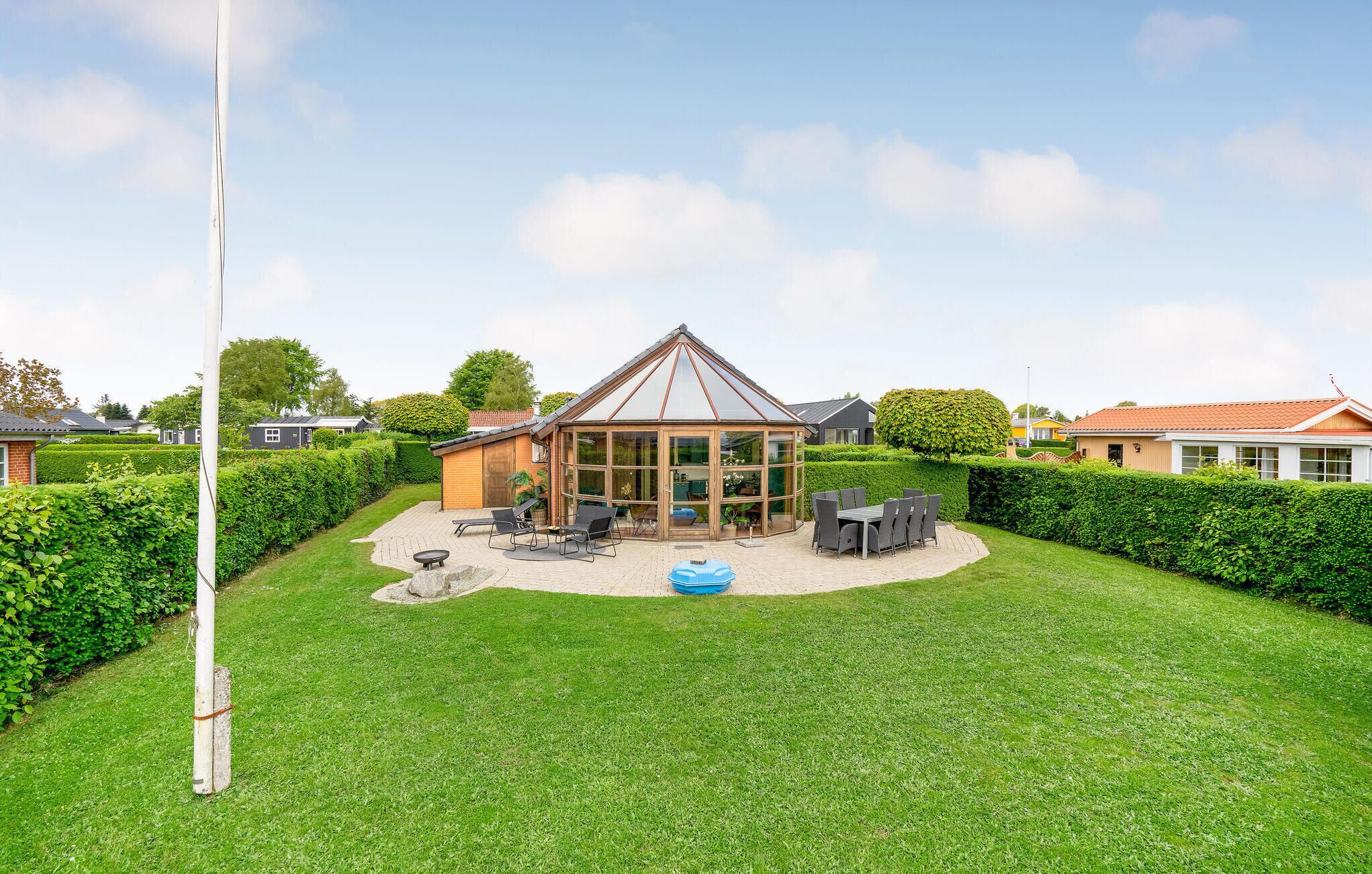 A house with a conservatory, a patio with outdoor furniture, and a well-maintained lawn.