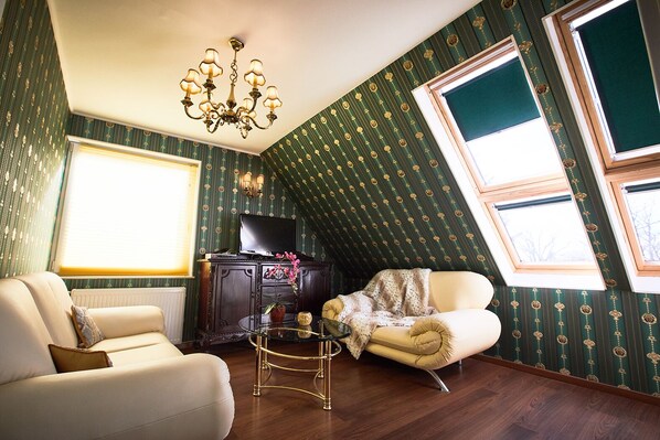 A room with a high ceiling, a chandelier, a television on a cabinet, and a window with a view of trees.