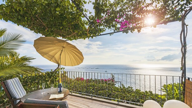 Une terrasse en bois avec une table et des chaises, un grand parasol et une vue sur la mer.