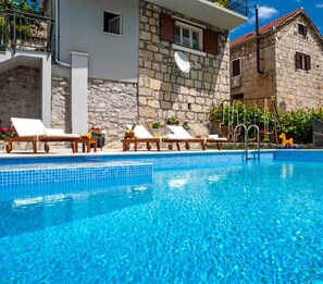 A pool area with lounge chairs and a stone building in the background. - * NEW * Charming stone house Duje with heated pool and jaccuzi (Svinisce)