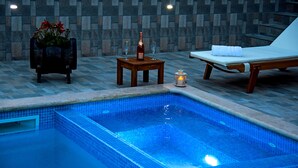 Ein Poolbereich mit einer gefliesten Poolanlage, einer Liege, einem kleinen Tisch mit einer Flasche und Gläsern sowie einem dekorativen Blumentopf.