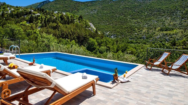 Ein Poolbereich mit Liegestühlen und Blick auf eine Berglandschaft.