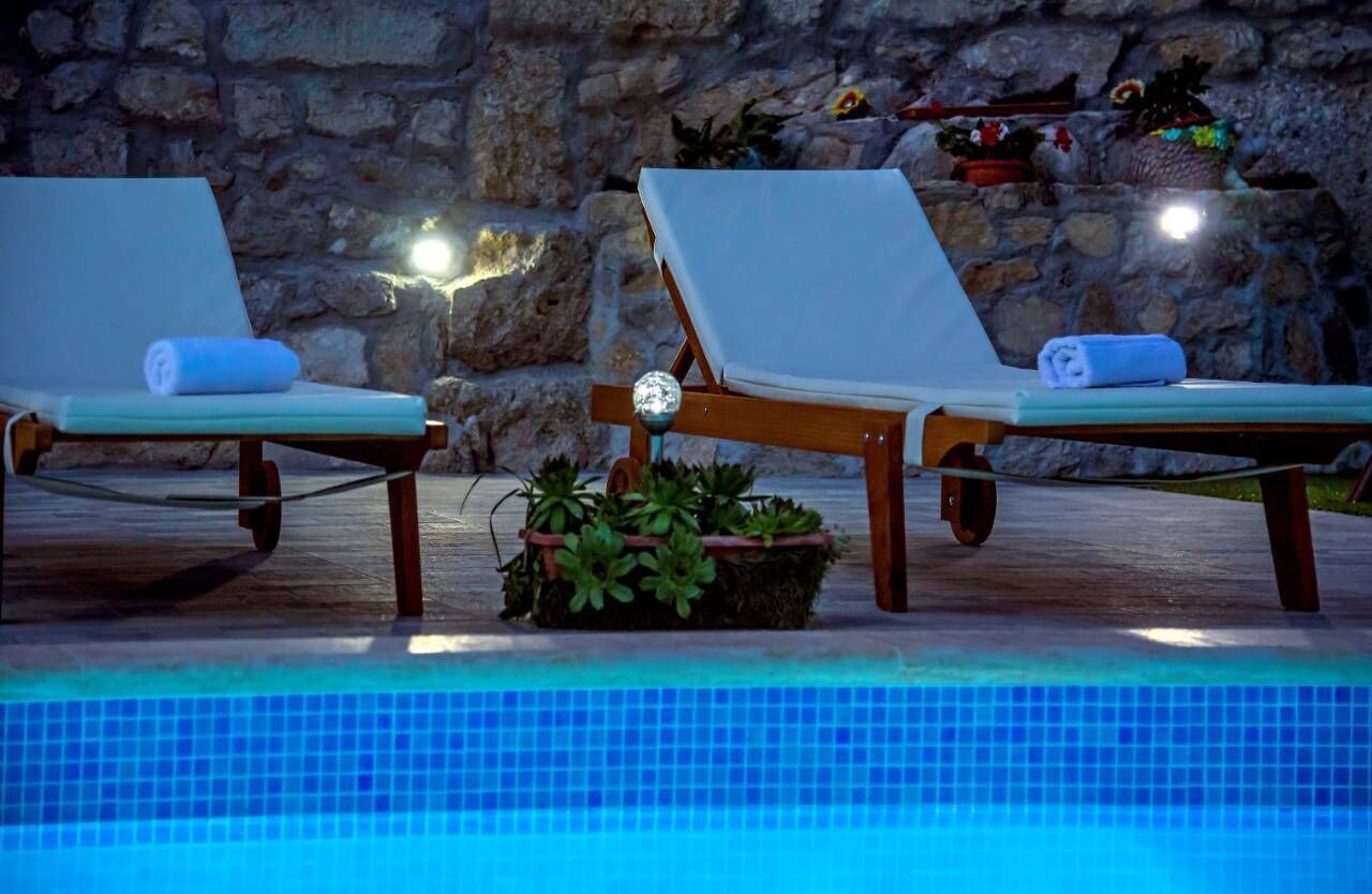 Dos sillones de descanso junto a una piscina, con un muro de piedra y plantas en macetas al fondo.