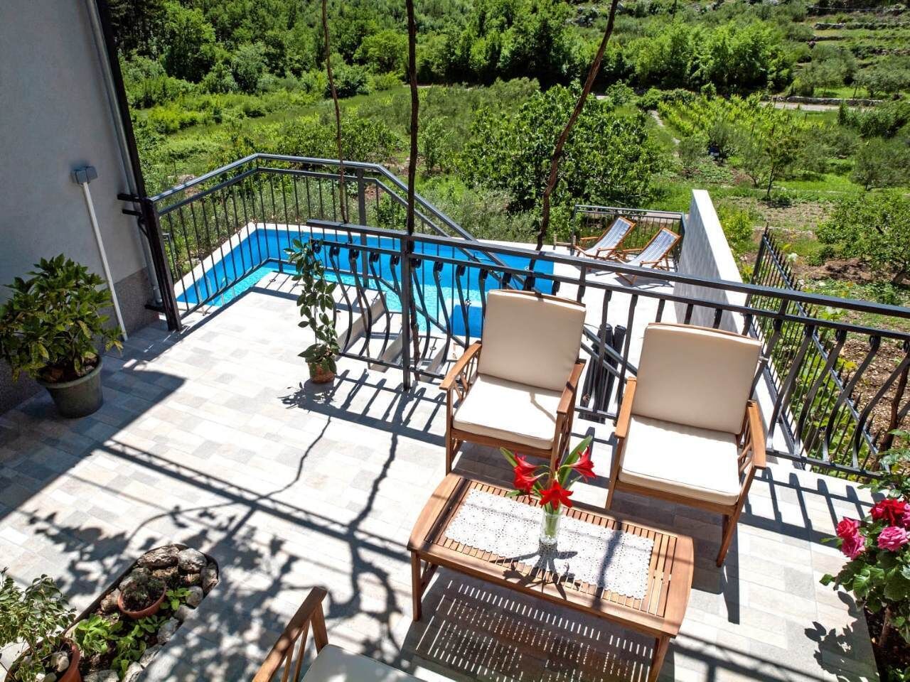 A balcony with a pool, two chairs, a table, and potted plants.