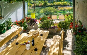 A wooden table set with wine glasses, a bottle, and a fruit platter, surrounded by potted plants and a view of a garden. - * NEW * Charming stone house Duje with heated pool and jaccuzi (Svinisce)