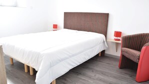 A neatly arranged bedroom with a large bed, a chair, and a small table with a lamp.
