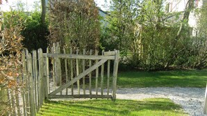 A wooden gate in a garden with a gravel path and green grass. - Modern house, 6 persons, 3 bedrooms, 2 bathrooms, smoke free, TOP location (De Cocksdorp)