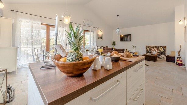Una cocina moderna con una isla de madera, armarios blancos y un ventanal con cortinas traslúcidas.