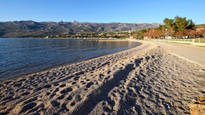 Una playa con huellas en la arena, cielo despejado y montañas al fondo.