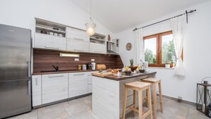 Una cocina moderna con refrigerador de acero inoxidable, armarios blancos, una isla de madera y una ventana con cortinas.