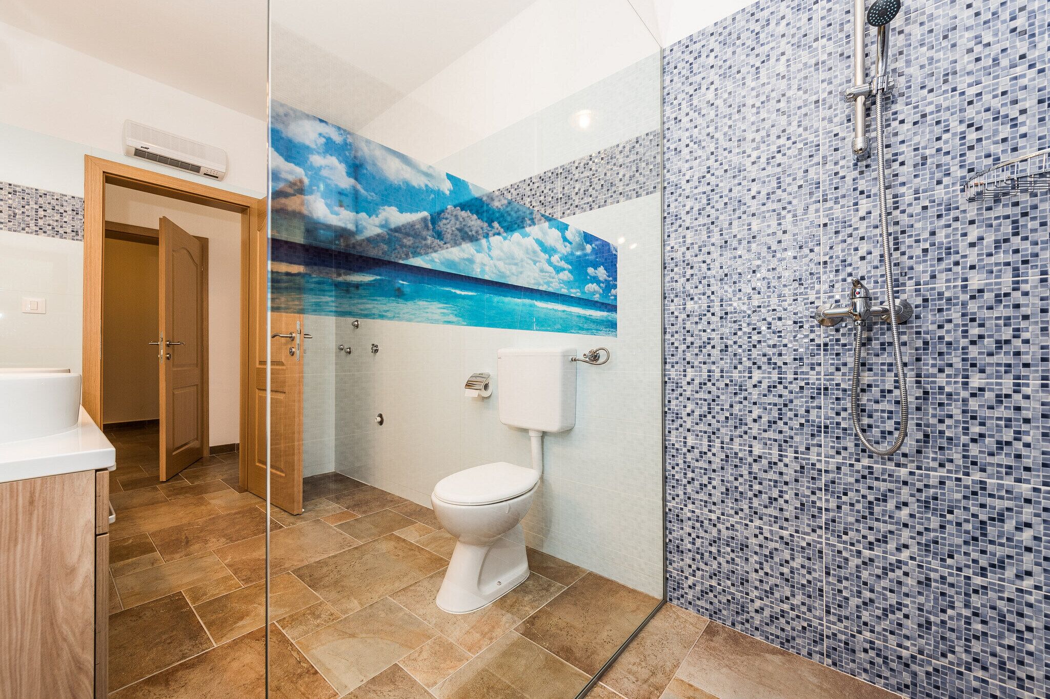 A bathroom with a glass shower enclosure, a toilet, and a tiled wall with a mosaic pattern.