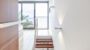 Et moderne interiør med en trappe op til en balkon med udsigt til palmer.