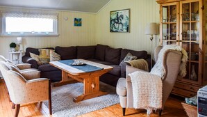 Un salon chaleureux avec un canapé marron foncé, une table basse en bois et un fauteuil de couleur claire. On aperçoit, au fond, un meuble en bois doté de portes en verre.