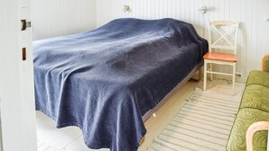 Un lit simple recouvert d’une couverture bleu foncé, dans une pièce aux murs blancs et au plancher en bois.