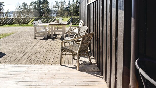 Une terrasse en bois avec des meubles d’extérieur, notamment une table et des chaises, et un bâtiment dont le revêtement extérieur est constitué de panneaux verticaux.