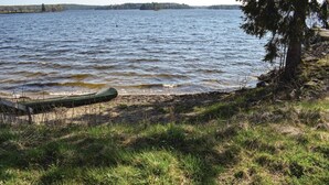 Un lac paisible, avec un canoë sur la rive, entouré d’une étendue herbeuse et d’un arbre.