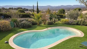 Una piscina con bordo curvo, circondata da prato ben curato e diverse siepi.