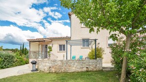 Una casa a due piani con un ingresso in muratura, un portico coperto e un giardino con un albero e fiori.