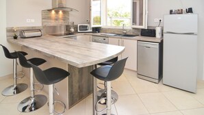 Una cucina moderna con isola centrale, sgabelli da bar, lavastoviglie, frigorifero e una finestra che offre luce naturale.
