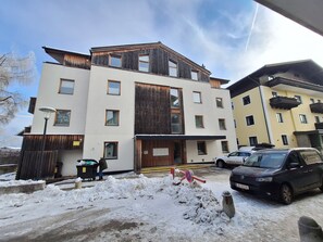 A multi-story hotel with a modern design, featuring a mix of wooden and white facades, and a parking area with snow on the ground.