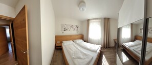A hotel room with two beds, wooden headboards, a small desk, a chair, and a large mirror.