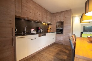 A modern kitchen with wooden cabinets, a built-in oven, and a dining area with a table and chairs.