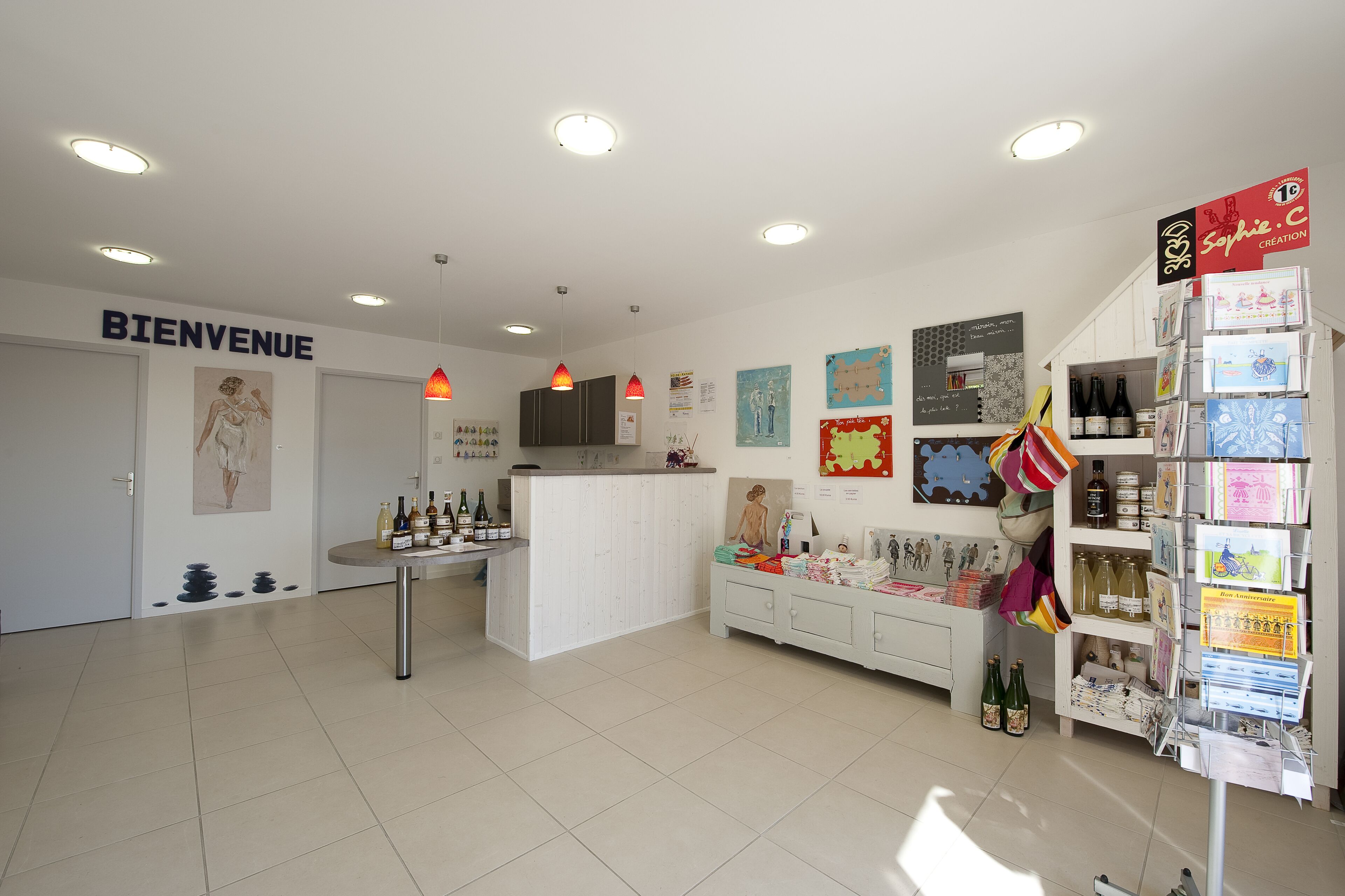 A modern interior with a reception area, a counter with bottles, and a display of books and postcards.