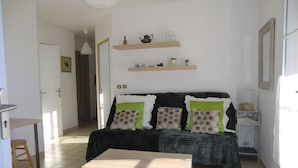A living room with a sofa, a coffee table, and a TV stand. There are two shelves above the sofa with decorative items.