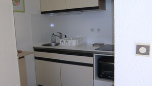 A compact kitchen with white cabinets, a sink, a kettle, and a microwave.