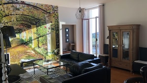 Un salon doté d’une grande fenêtre, d’un canapé en cuir noir, d’une table basse en verre et d’un meuble avec des portes en verre.