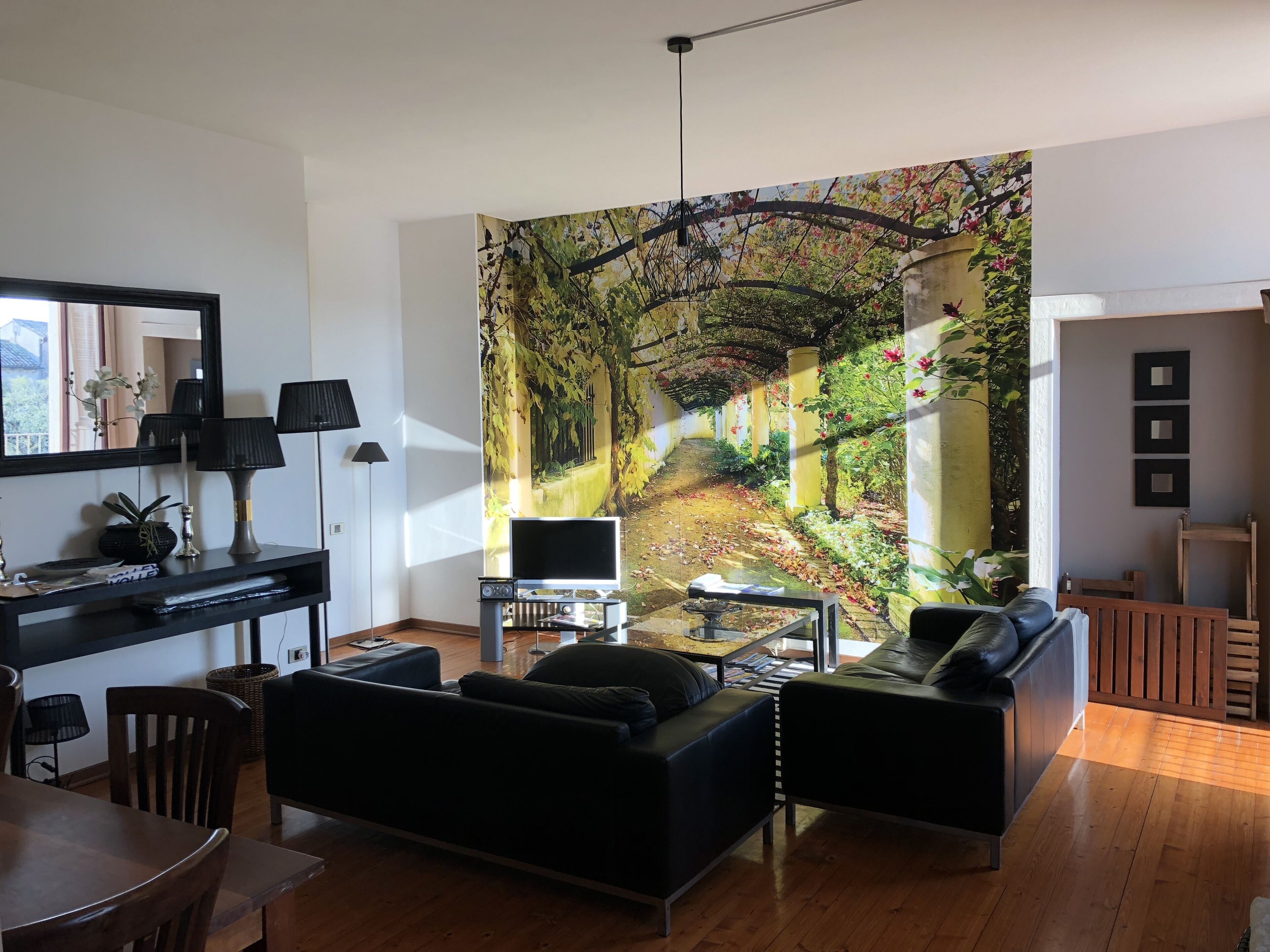 Ett modernt vardagsrum med en stor väggmålning, en svart soffa, ett soffbord och en TV-bänk.