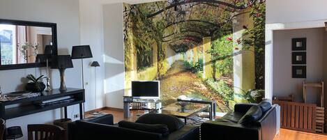 Ett modernt vardagsrum med en stor väggmålning, en svart soffa, ett soffbord och en TV-bänk.