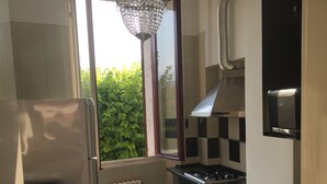 Une cuisine compacte équipée d’un lave-linge, d’un réfrigérateur, d’un évier, d’une cuisinière et d’une fenêtre donnant sur un espace verdoyant.
