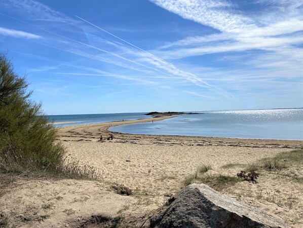 Uma praia com céu claro, areal arenoso e uma ilha ao longe.
