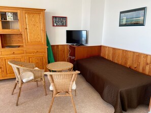 Quarto com cama, televisão, armário de madeira e cadeiras de vime.