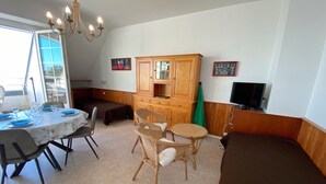 Un comedor con una mesa dispuesta para dos personas, una silla de mimbre, un armario y un televisor sobre un mueble.