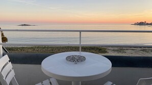 Una mesa redonda con un centro decorativo, dos sillas blancas y vista al océano al atardecer.
