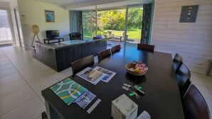 Ein modernes Wohnzimmer mit großem Esstisch, bequemen Sitzgelegenheiten und Blick auf den Garten durch Glastüren.