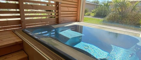 A hot tub area with wooden steps leading up to it, a window with a view of greenery, and a metal roof structure.