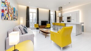 A modern living room with a sofa, coffee table, and yellow chairs. There is a kitchen area with a white countertop and appliances. - Clic 20-2121-Beautiful apartment on rue d'Antibes (Cannes)