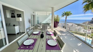 A balcony with a dining table set for two, a sofa, and a potted plant. - 9 - Apartment in Reserva de higueron , Benalmadena (Benalmádena)