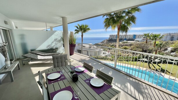 A balcony with a dining table set for four, overlooking a pool and a coastal view. - 9 - Apartment in Reserva de higueron , Benalmadena (Benalmádena)
