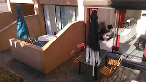 A small outdoor seating area with a table and chairs, a blue umbrella, and a black coat hanging on a hook. - Santa Lucia, Unit 357 (Santa-Lucia-Di-Moriani)