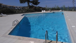 A rectangular swimming pool with clear blue water, surrounded by a tiled deck. There are lounge chairs and a small table on the deck. - Santa Lucia, Unit 357 (Santa-Lucia-Di-Moriani)